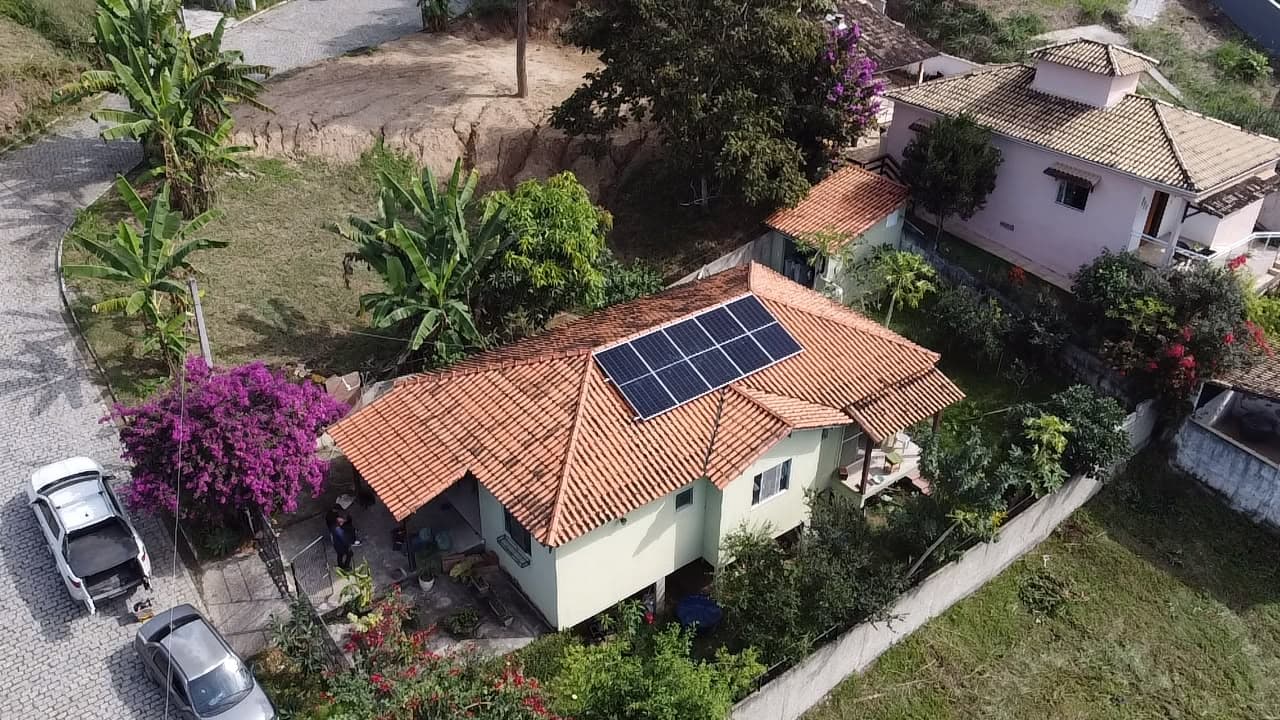 Vista aérea de casa com telhado de telhas e painéis solares, cercada por vegetação