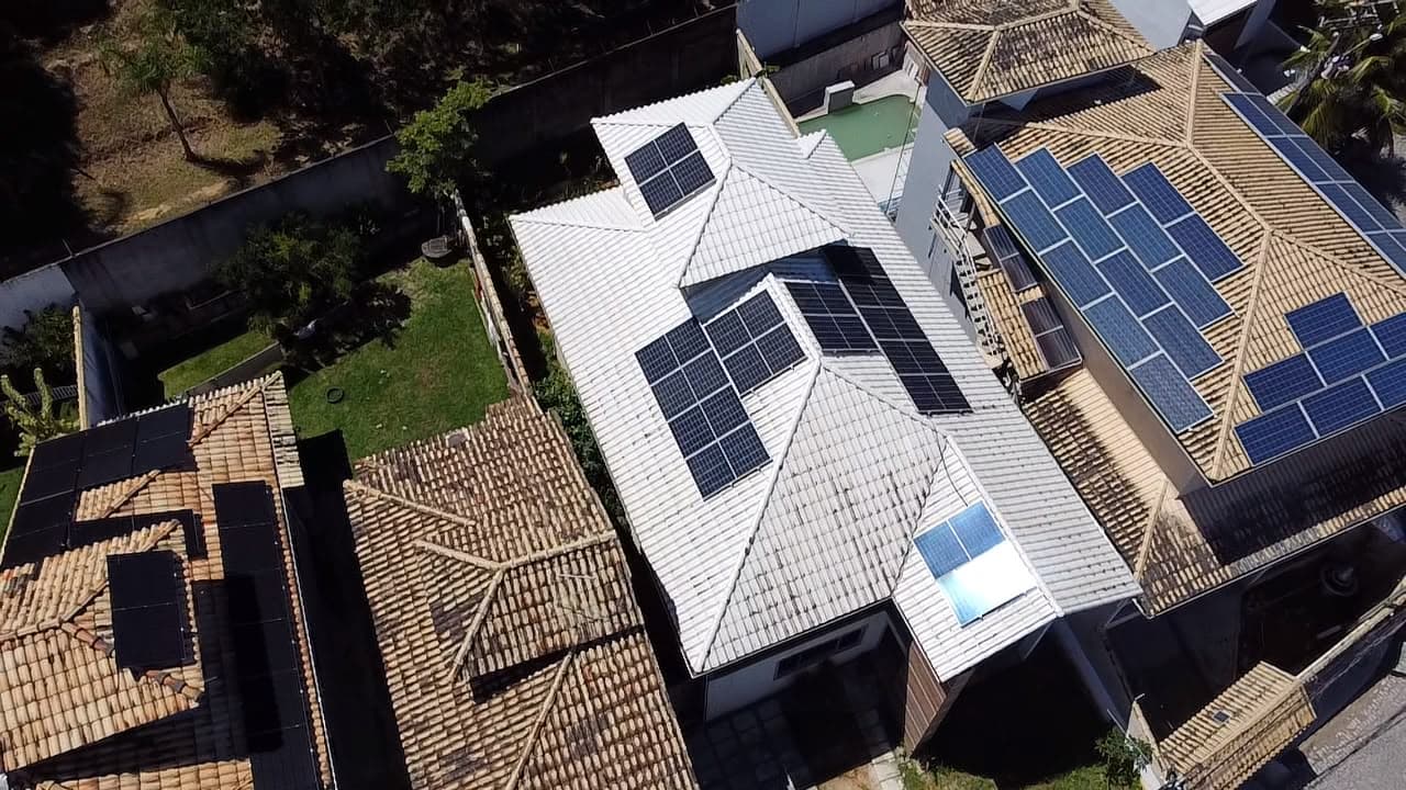 Vista aérea de casas geminadas com painéis solares em telhados brancos, uma delas com piscina