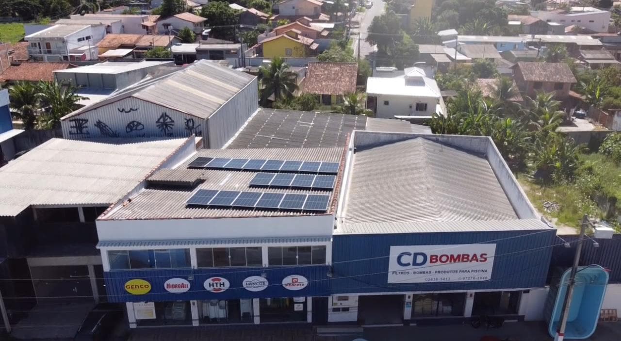 Vista aérea de loja com painéis solares no telhado, fachada com letreiro de comércio