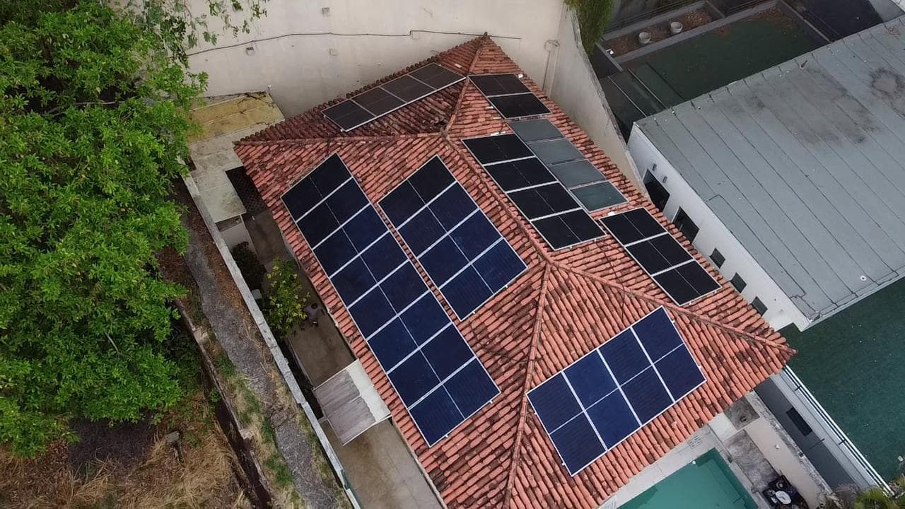 Vista aérea de casa com telhado de telhas e painéis solares distribuídos em diferentes águas do telhado