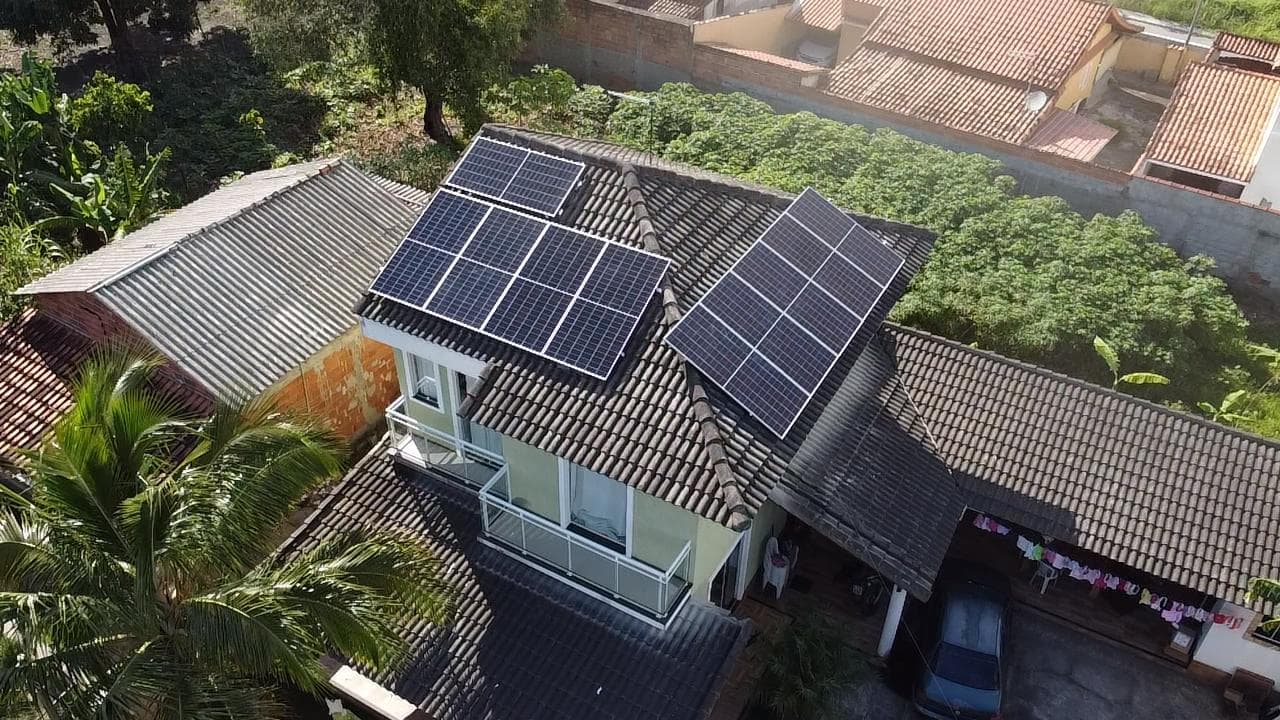 Vista aérea de casa de dois andares com painéis solares no telhado, cercada de vegetação