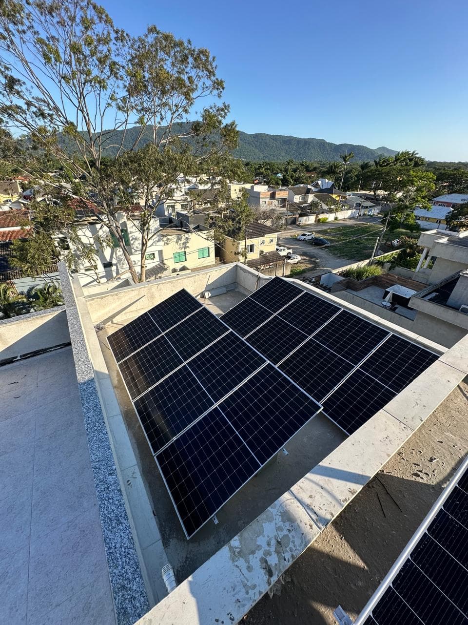 Vista de cima de painéis solares recém-instalados num telhado, com vista para montanhas ao fundo